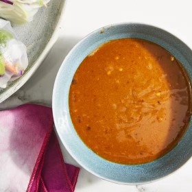 Eine Schüssel Erdnuss-Sauce auf einem Tisch, umgeben von frischen Zutaten. Ideal für gesunde Mahlzeiten und Rezepte.